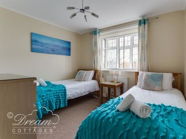 A bedroom with two single beds each with turquoise throws and pillows and a wooden bedside table with lamps and a window at Redcliff View Lodge in Weymouth