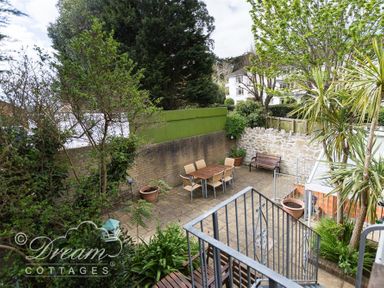 A patio with a dining table and chairs surrounded by trees and plants at Redcliff View Lodge in Weymouth