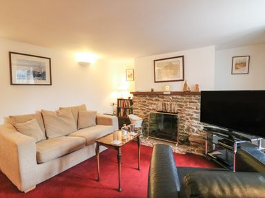 A living room with two sofas a wooden table a stone fireplace and a television at River Cottage in Burton Bradstock