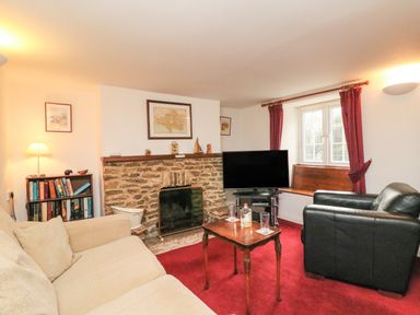 A living room with a beige sofa black armchair stone fireplace television and red carpet at River Cottage in Burton Bradstock