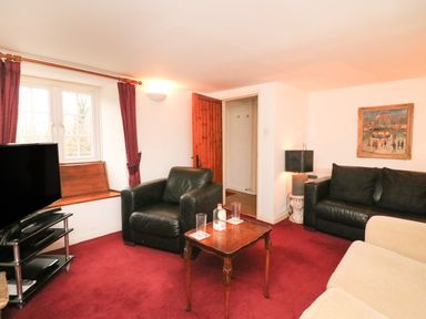 A living room with black leather chairs a wooden table a television on a stand and red carpet at River Cottage in Burton Bradstock