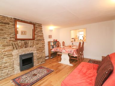 A dining area with table and chairs next to a stone fireplace and a red sofa at River Cottage in Burton Bradstock