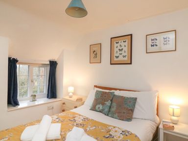 A bedroom with a bed with floral bedding and two bedside tables with lamps at River Cottage in Burton Bradstock