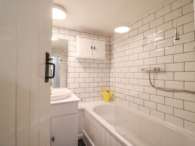 A bathroom with a bathtub shower and a white cabinet on the wall at River Cottage in Burton Bradstock
