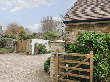 A paved courtyard with wooden gates stone walls and green plants at River Cottage in Burton Bradstock
