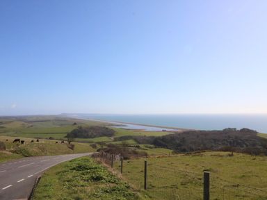A coastal landscape with a curving road, green fields, grazing cows, and the sea in the distance at River Cottage in Burton Bradstock