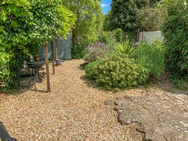 A garden area with gravel pathway metal table and chairs and green plants at River Cottage in Burton Bradstock