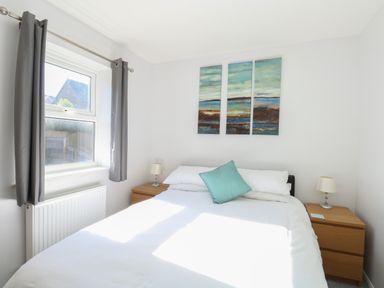 A bedroom with a double bed white bedding two wooden bedside tables lamps and a three-piece wall painting at Rockpools in Weymouth