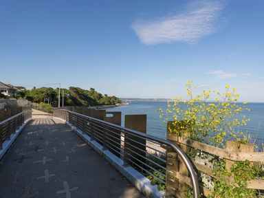 A coastal pathway with a metal railing overlooking the sea and yellow flowers on a wooden fence at Rockpools in Weymouth