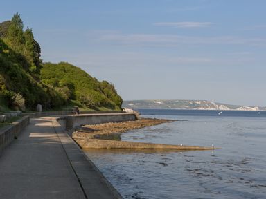 A coastal pathway beside the sea with greenery on one side and cliffs in the distance at Rockpools Weymouth
