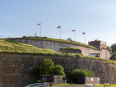 A fort with multiple flags on poles and grass on its walls at Nothe Fort in Weymouth