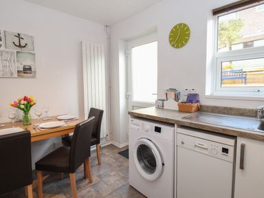 A kitchen with a dining table set with plates and glasses a washing machine dishwasher sink window and door at Rockpools in Weymouth