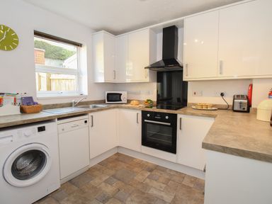A kitchen with white cabinets appliances and a window at Rockpools in Weymouth