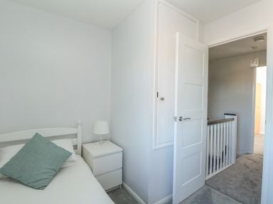 A small bedroom with a single bed a bedside table with a lamp and an open door showing a hallway at Rockpools in Weymouth