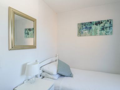 A bedroom with a single bed white bedside table and lamp and a painting on the wall at Rockpools in Weymouth