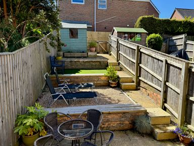 A tiered backyard with patio furniture two lounge chairs wooden sheds and potted plants at Rockpools in Weymouth