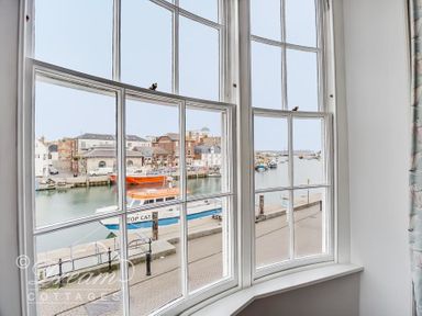 A view of boats and waterfront buildings through large curved window at Safe Harbour Brewers Quay harbour