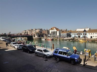 A street with parked cars beside a river and buildings across the water at Safe Harbour in Brewers Quay harbour