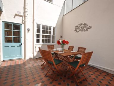 An outdoor patio with a wooden table and six chairs a vase with flowers on the table and a blue door at Safe Harbour Brewers Quay harbour