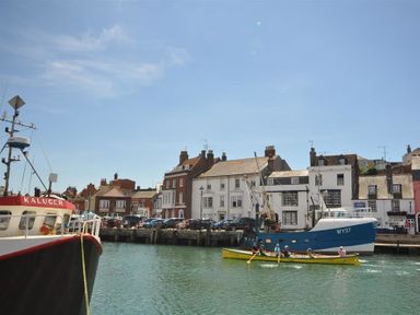 A harbor with boats and a rowboat with people near a quay with buildings at Safe Harbour in Brewers Quay harbour