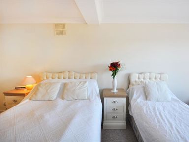 A bedroom with two beds separated by a nightstand with a vase of flowers at Sanjernin in Swanage