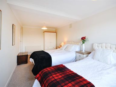 A bedroom with two single beds a wardrobe a bedside table with a lamp and flowers at Sanjernin in Swanage