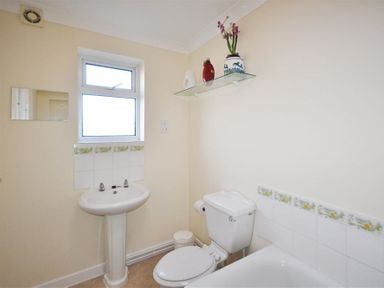 A bathroom with a pedestal sink under a window a toilet next to a bathtub and a glass shelf with vases above the toilet at Sanjernin Swanage
