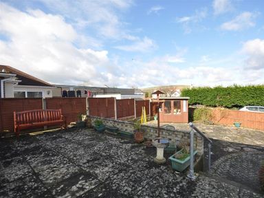 A backyard with a wooden bench plants a birdbath a small wooden shed and a fence at Sanjernin in Swanage