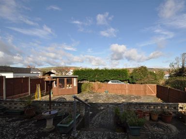 A backyard with a paved patio area a birdbath potted plants wooden fencing and a garden shed at Sanjernin in Swanage