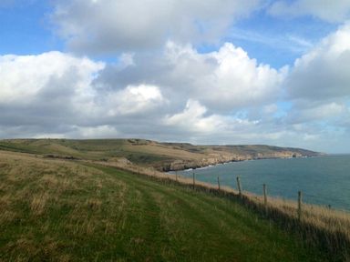 A coastal landscape with grassy cliffs and a path along the edge of the sea at Sanjernin in Swanage