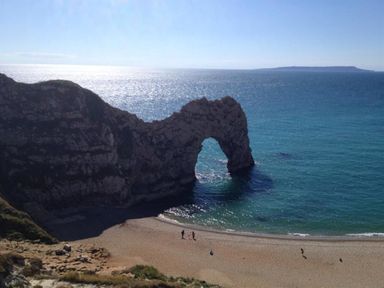 A natural limestone arch on a beach with people walking near the shore at Sanjernin in Swanage