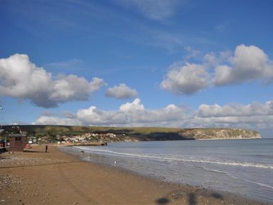 A beach with sand and pebbles next to a calm sea under a blue sky with clouds at Sanjernin in Swanage