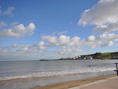 A beach with waves and a pier with buildings and hills in the background at Sanjernin in Swanage