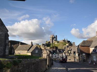 A street with stone buildings and a castle on a hill in the background at Sanjernin in Swanage