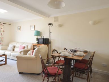 A living room with a dining table set for four and beige sofas with cushions at Sanjernin Swanage