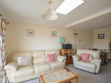A living room with cream leather sofas a wooden coffee table a side cabinet with a turquoise lamp and a stereo at Sanjernin in Swanage