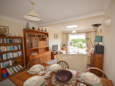 A dining table set with plates and glasses in a living room with bookshelf and wooden cabinet at Sanjernin in Swanage