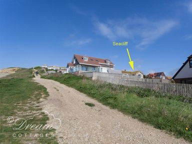 A dirt path leading uphill with grass on both sides and houses with fences on the right side at Seacliff West Bay