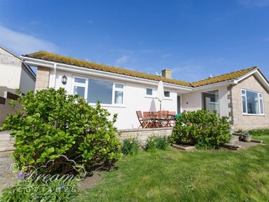 A single story house with a patio table and chairs in a garden at Seacliff in West Bay