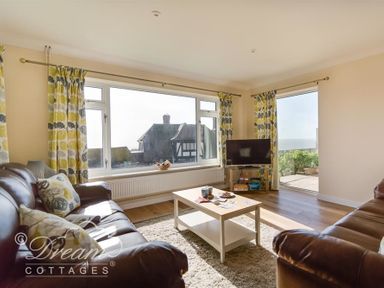 A living room with two leather sofas a coffee table a television and large windows showing houses and a garden at Seacliff in West Bay