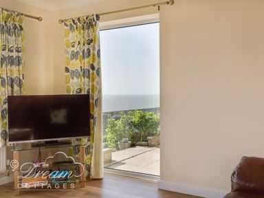 A corner of a room with a television on a glass stand and a large window showing a view of the sea at Seacliff in West Bay