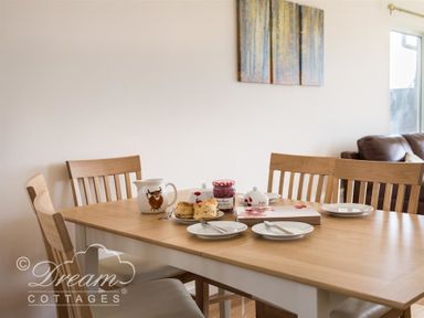 A dining table set with plates knives scones a jar of jam a jug and a sugar bowl with wooden chairs at Seacliff in West Bay