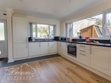 A kitchen with white cabinets wooden floor and large windows showing an outdoor shed at Seacliff in West Bay