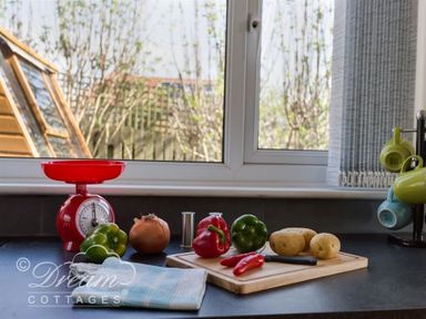 A kitchen counter with a red kitchen scale green and red peppers an onion potatoes a knife a cutting board and hanging colorful mugs at Seacliff in West Bay