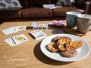 A wooden table with playing cards a plate of biscuits and two mugs in a living room at Seacliff in West Bay