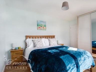A bedroom with a wooden bed frame blue blanket bedside tables and a closet at Seacliff in West Bay