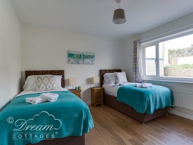 A bedroom with two single beds bedside tables with lamps a window and wooden floor at Seacliff in West Bay