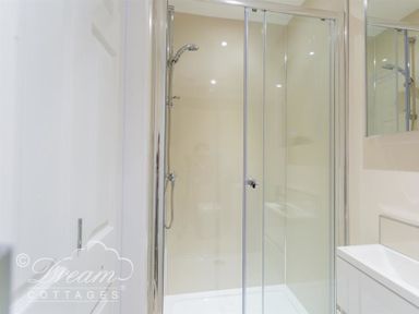 A shower with glass doors and a sink with a mirror in a bathroom at Seacliff in West Bay