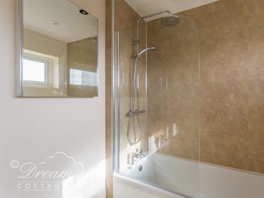 A bathroom with a bathtub shower combination a glass shower screen a wall-mounted showerhead and a mirror at Seacliff in West Bay