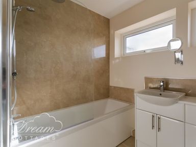 A bathroom with a bathtub and shower head next to a sink with a cabinet below and a small window above at Seacliff in West Bay